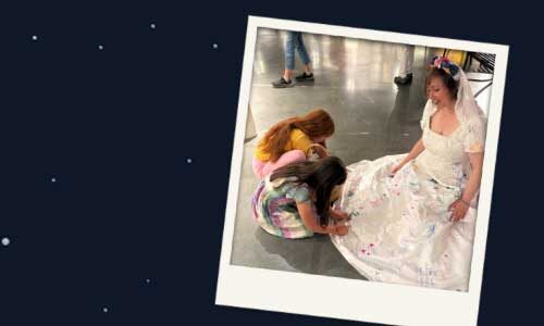 Marleen at the Sooke Fine Arts Show in 2025. Two girls are drawing art on her wedding dress.